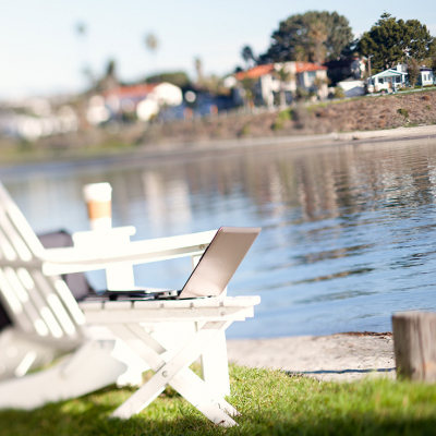 Laptop on a table next to an Adirondack chair, overlooking water