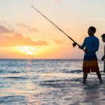 Father and Son fishing on the beach at sunset