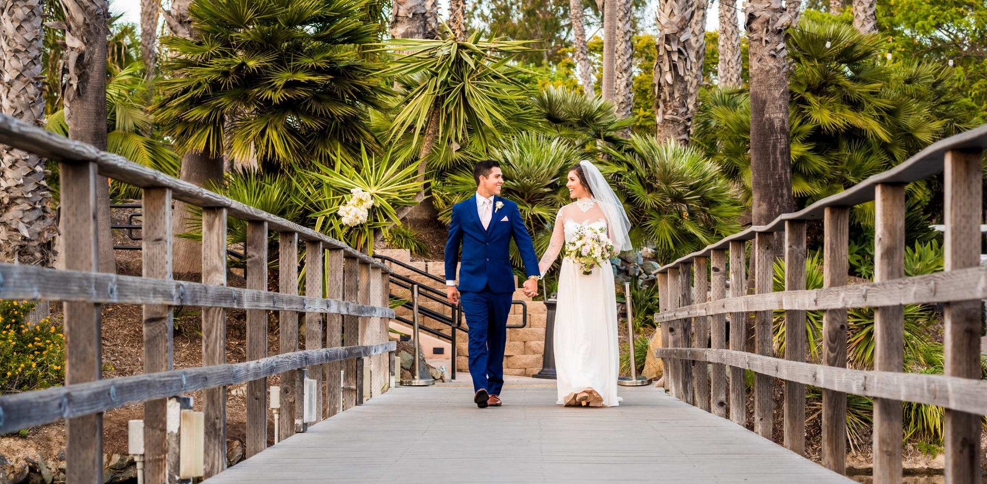 bride and groom walking across bridge with tropical setting